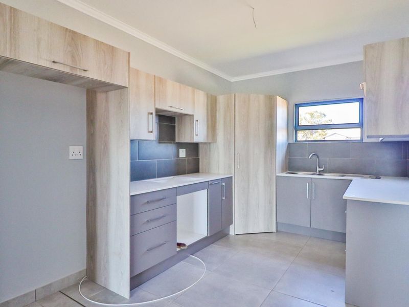 A modern, empty kitchen featuring light wood-tone cabinetry, grey tiled backsplash, and neutral floor tiles, offering a clean and functional space.