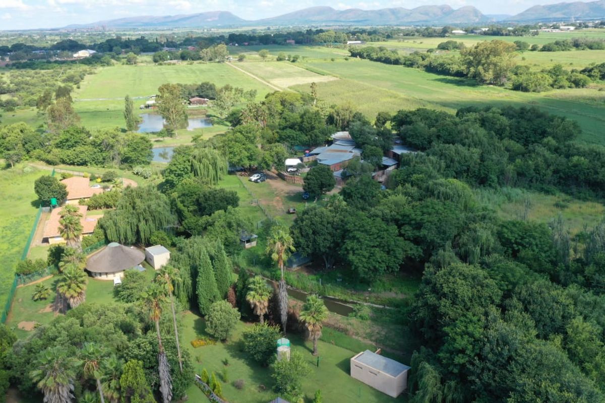 Aerial view of a sprawling farm property featuring mature trees, landscaped grounds, multiple structures, and open fields in a rural setting.
