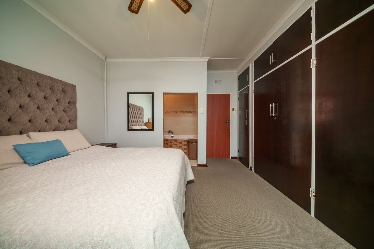 Spacious bedroom featuring built-in dark wood cupboards, carpeted flooring, a ceiling fan, and direct access to an en-suite bathroom.