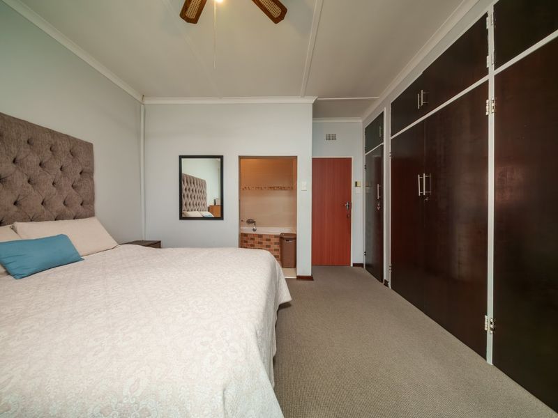 Spacious bedroom featuring built-in dark wood cupboards, carpeted flooring, a ceiling fan, and direct access to an en-suite bathroom.