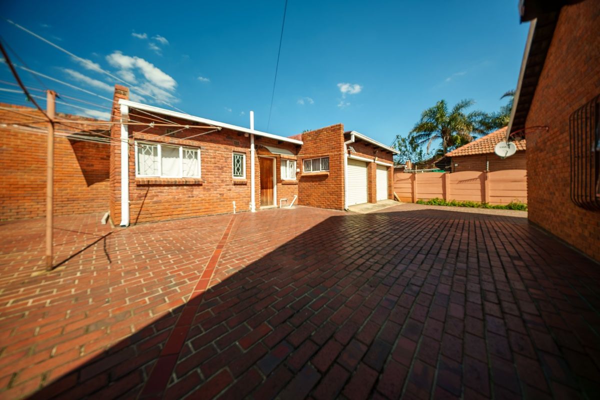 Rear exterior view featuring a spacious brick-paved courtyard, double garage access, and traditional face-brick construction.