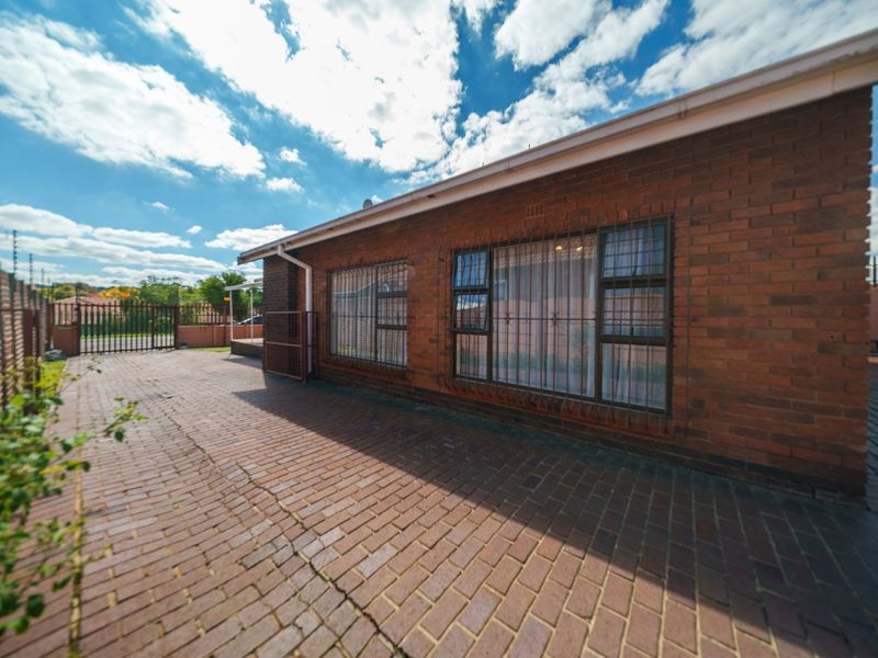 A view of the rear exterior featuring brick paving, a face brick facade, and secure perimeter fencing.