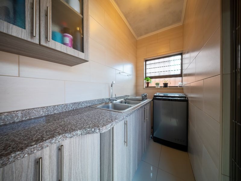 A functional laundry room featuring built-in cabinetry, a granite countertop with a stainless steel sink, and full-height wall tiling.