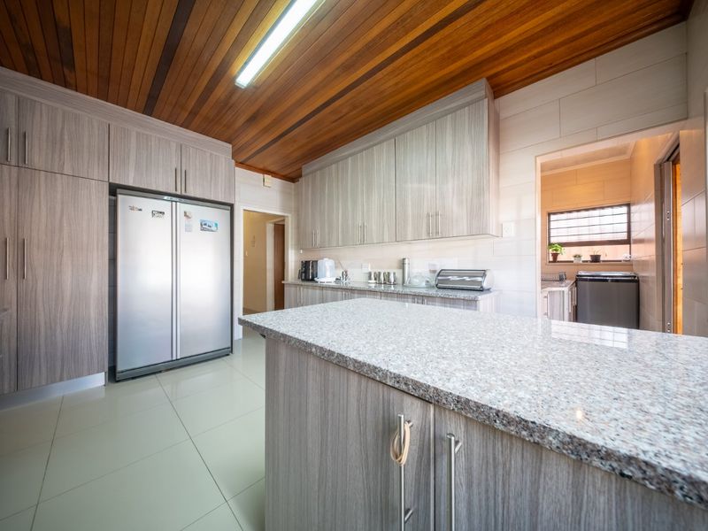 Modern kitchen featuring granite countertops, extensive built-in cabinetry, and a distinctive timber-clad ceiling, with an adjacent scullery area.