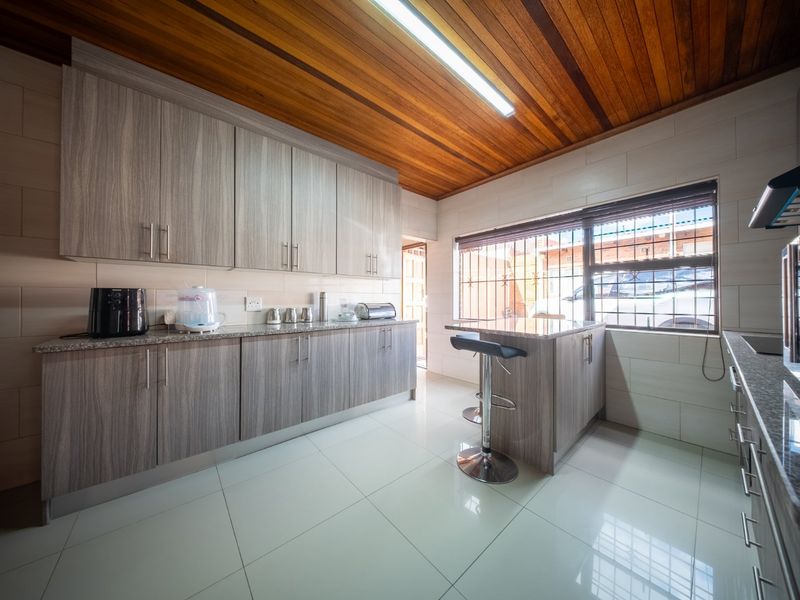 Modern kitchen featuring wood-grain cabinetry, granite countertops, tiled flooring, and a distinctive timber-paneled ceiling with integrated lighting.