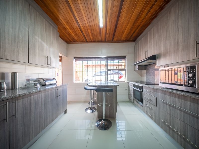 Modern galley-style kitchen featuring wood-grain cabinetry, granite countertops, built-in oven, extractor fan, and a distinctive timber-paneled ceiling with tiled flooring.