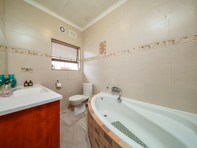 A functional bathroom featuring a built-in vanity, a tiled bathtub surround, and neutral wall tiling, though the ceiling shows signs of water damage.
