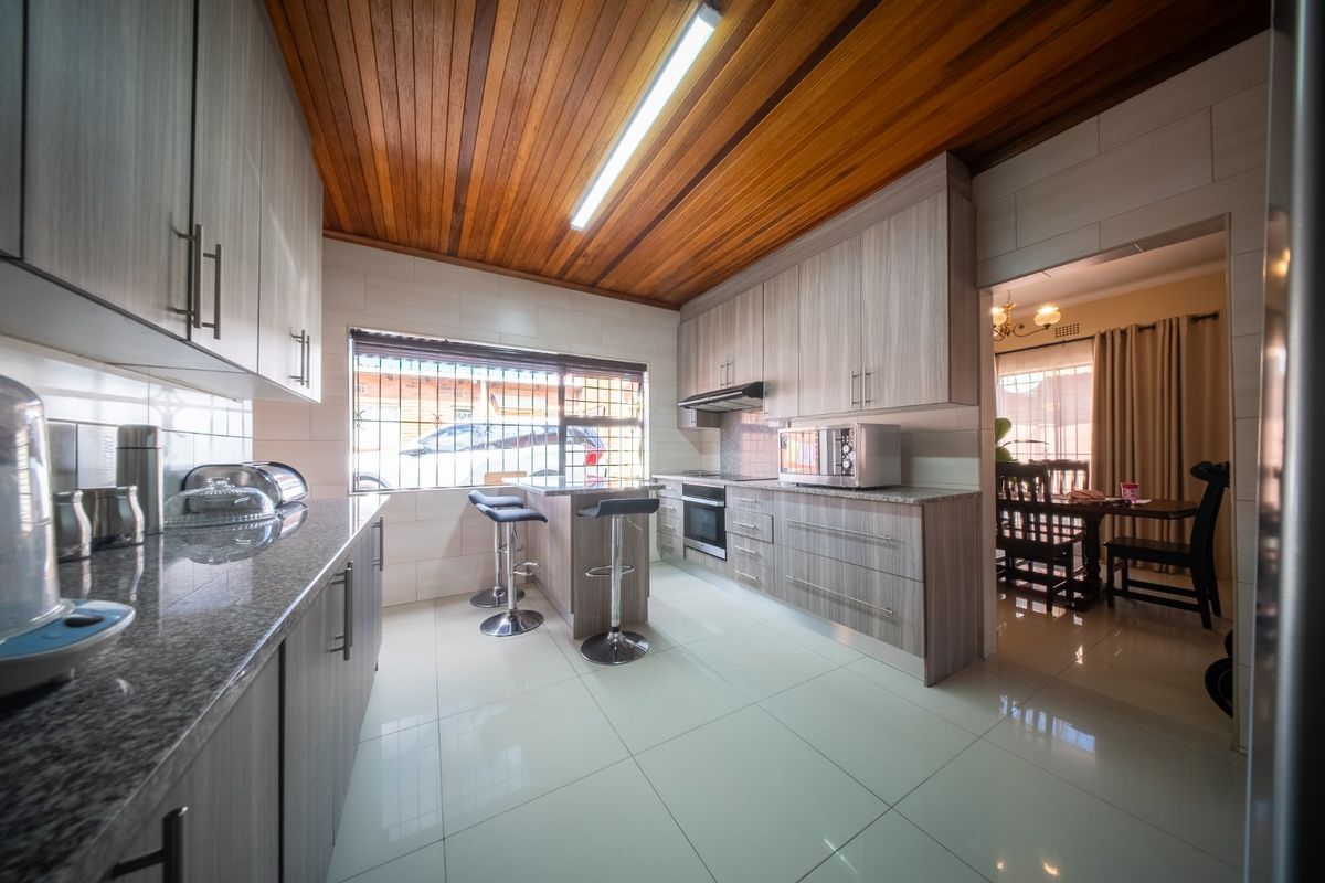 Modern kitchen featuring light wood-grain cabinetry, granite countertops, integrated oven, extractor fan, and a warm timber-paneled ceiling with tiled flooring.