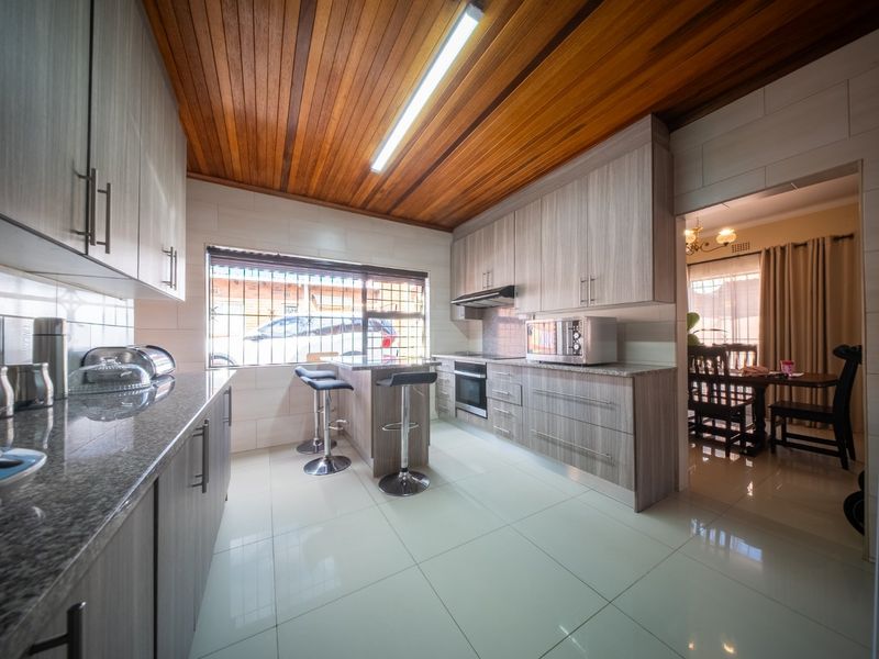 Modern kitchen featuring light wood-grain cabinetry, granite countertops, integrated oven, extractor fan, and a warm timber-paneled ceiling with tiled flooring.