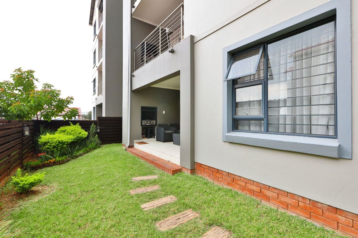 Rear view of the townhouse featuring a private garden, a covered patio with a built-in braai, and modern aluminium window frames.