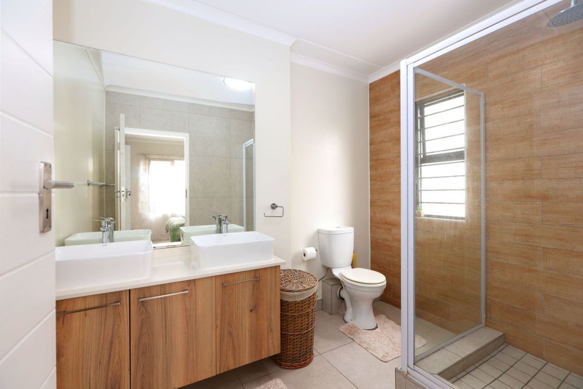 Modern bathroom featuring a double vanity with vessel sinks, a glass-enclosed shower, and contemporary wood-look wall tiling.