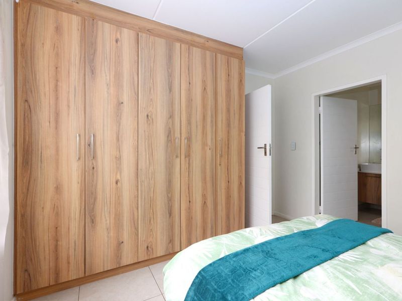 A well-maintained bedroom featuring modern wood-finish built-in cupboards and neutral tiled flooring, with direct access to an en-suite bathroom.