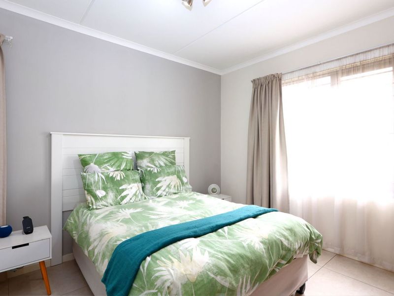 A bright and well-maintained bedroom featuring neutral wall tones, tiled flooring, and large windows with installed curtain rails.