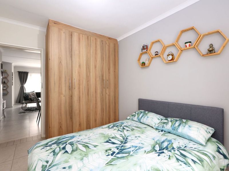 A well-maintained bedroom featuring a large built-in wooden wardrobe, neutral wall finishes, and tiled flooring, with a view into the adjacent living area.