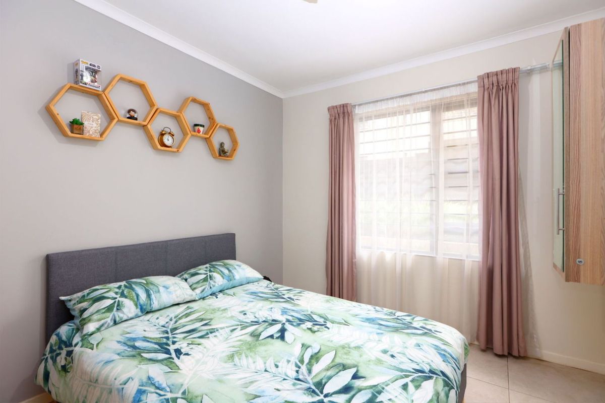 A well-maintained bedroom featuring tiled flooring, a built-in wardrobe, and a window fitted with security bars for added peace of mind.