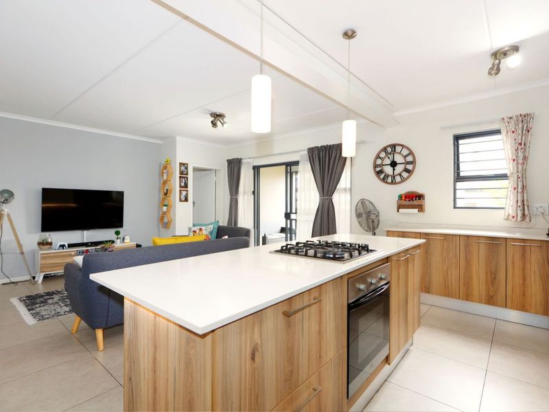 Modern open-plan living area featuring a kitchen island with a gas hob, built-in oven, stone countertops, and tiled flooring throughout.
