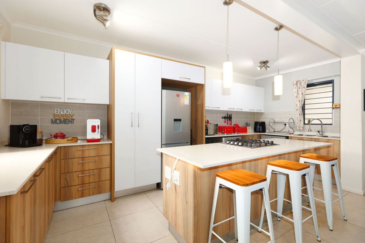 Modern kitchen featuring wood-grain and white cabinetry, stone countertops, a central island with a gas hob, and tiled flooring.