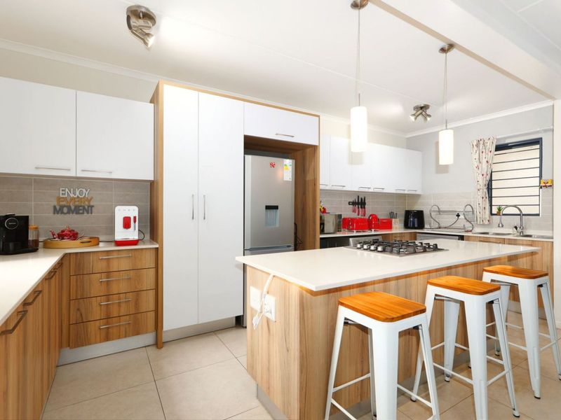 Modern kitchen featuring wood-grain and white cabinetry, stone countertops, a central island with a gas hob, and tiled flooring.