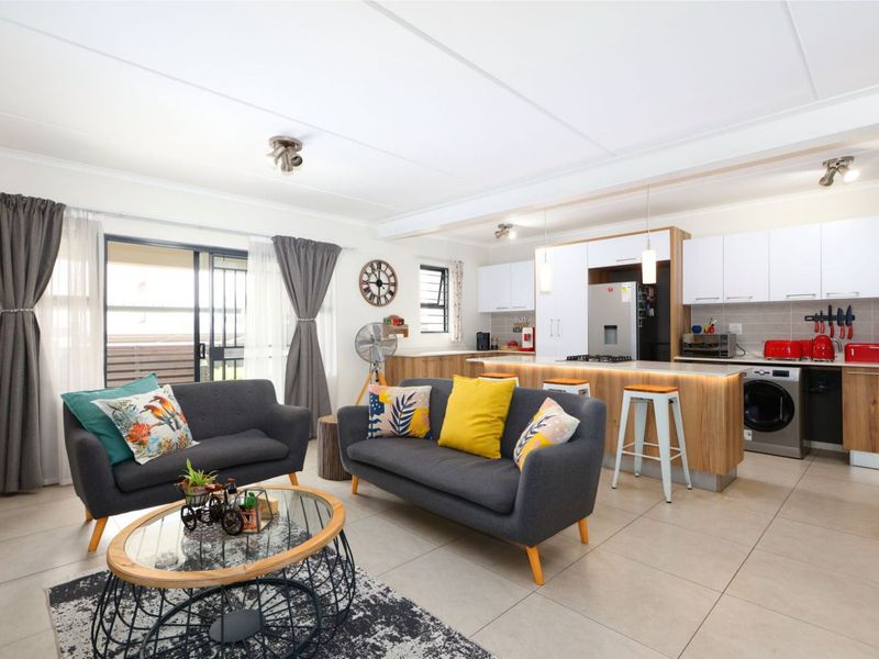 Modern open-plan living area featuring a contemporary kitchen with stone countertops, integrated appliances, and seamless flow to the outdoor patio through sliding doors.