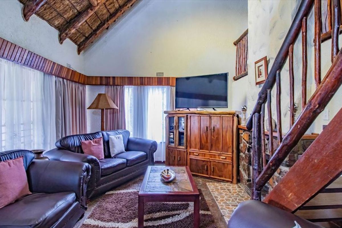 Cozy living room featuring a high vaulted thatched ceiling with exposed timber rafters, a stone fireplace, and a rustic timber staircase.