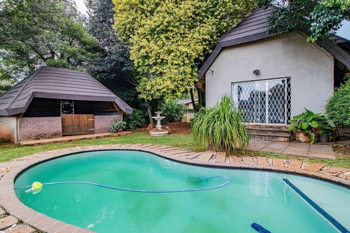 Outdoor pool area featuring a swimming pool with brick coping, a stone patio, and a secondary thatched structure set within a garden.