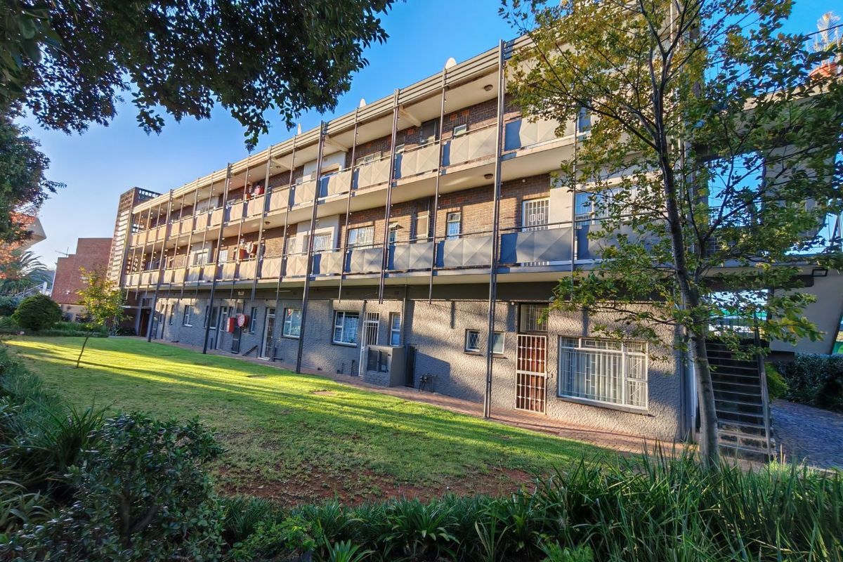 A multi-story apartment building exterior featuring brick facade, private balconies with metal railings, and a well-maintained communal lawn area.