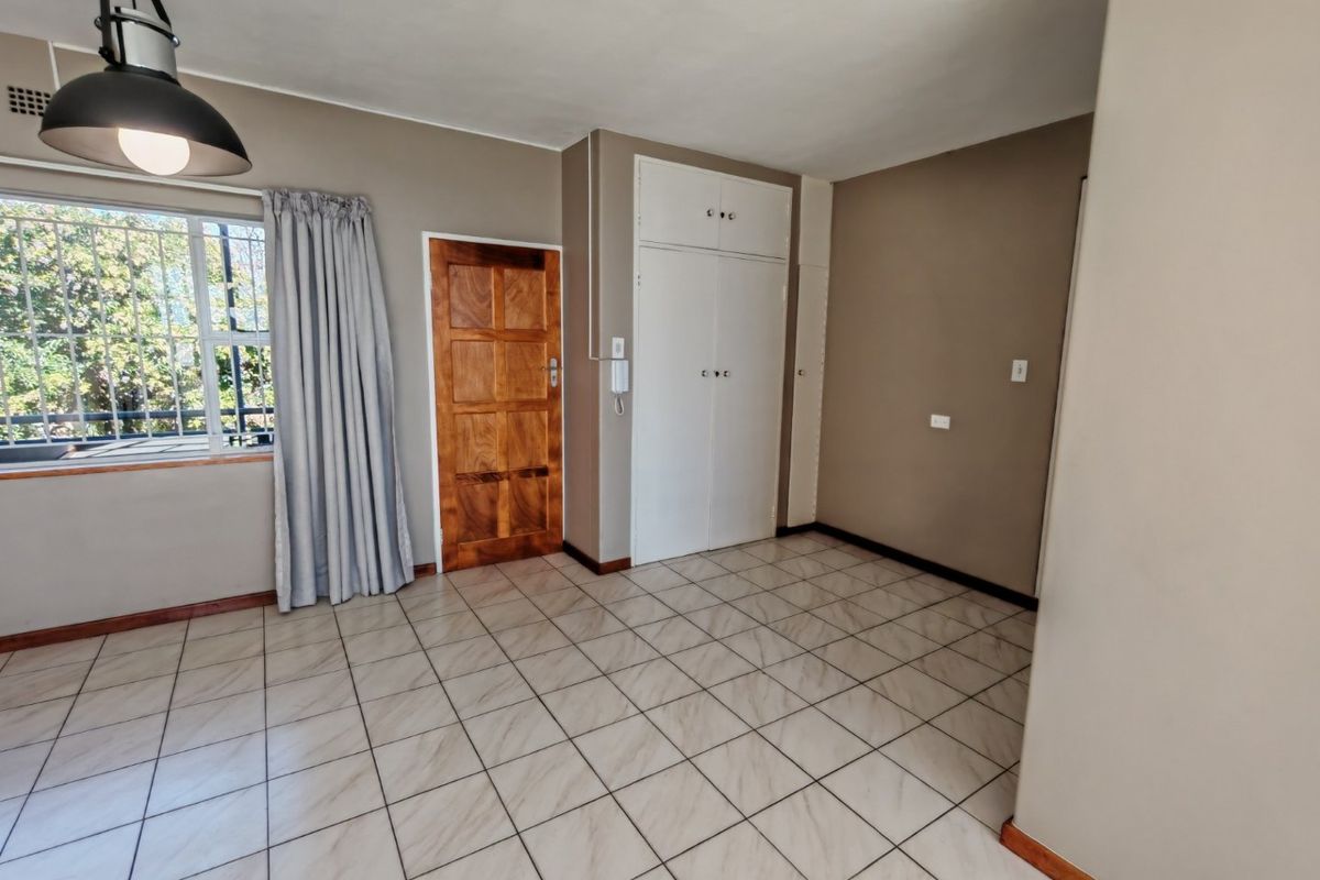 A clean, empty bedroom featuring tiled flooring, built-in cupboards, and a window with security bars, offering a neutral canvas for personalization.