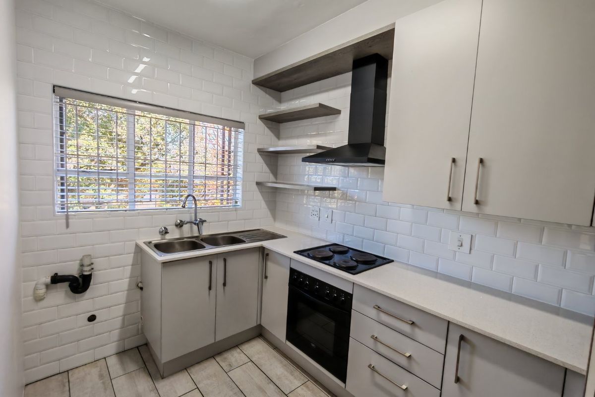 Modern kitchen featuring subway tile backsplash, stone countertops, built-in oven, electric hob, extractor fan, and ample fitted cabinetry with open shelving.