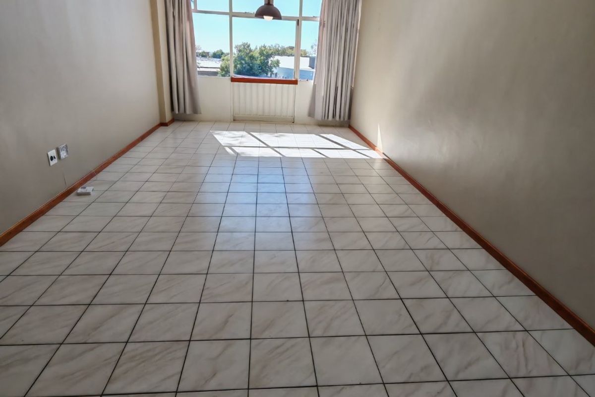 A spacious, empty living area featuring neutral tiled flooring, large windows providing natural light, and modern pendant lighting.