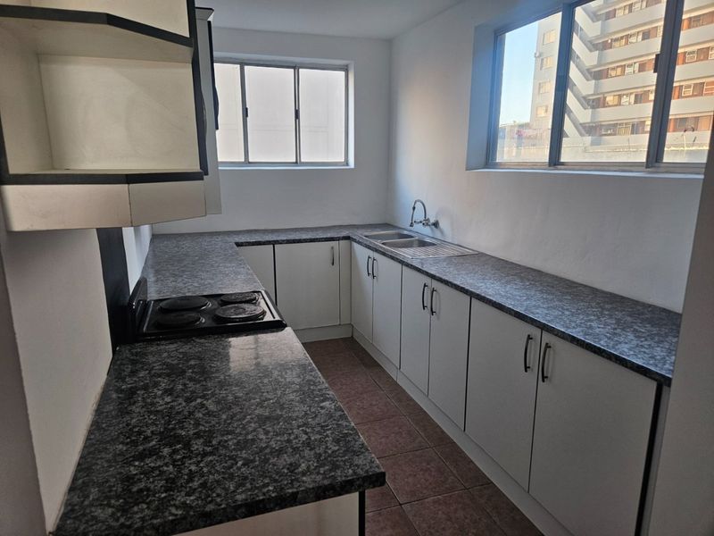 A functional kitchen featuring white cabinetry, dark laminate countertops, an integrated electric hob, and a double sink with tiled flooring.