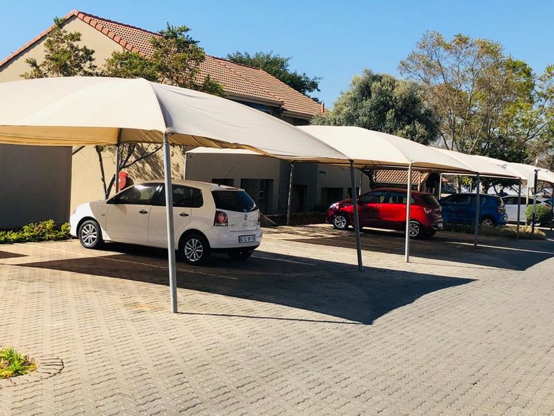 Exterior view of the apartment complex featuring a paved parking area with covered shade cloth carports.