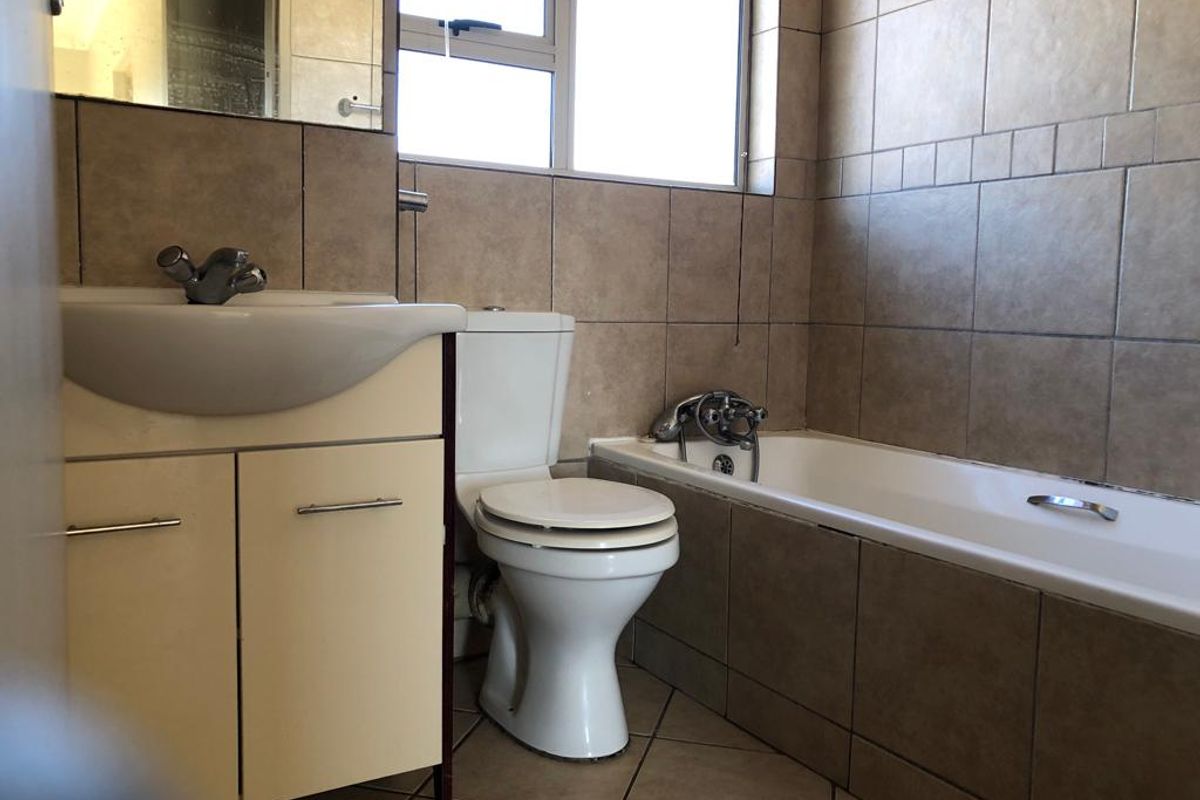 A functional bathroom featuring a vanity cabinet, toilet, and bathtub with neutral wall and floor tiling.