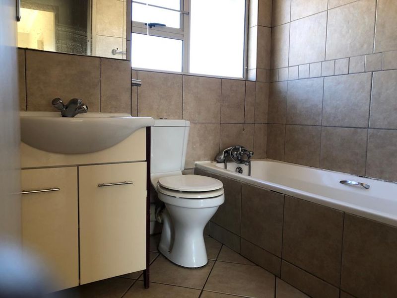 A functional bathroom featuring a vanity cabinet, toilet, and bathtub with neutral wall and floor tiling.