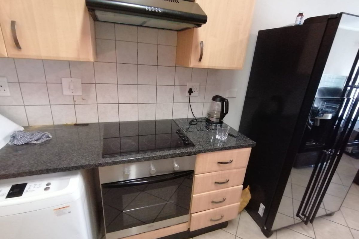 A functional kitchen featuring light wood cabinetry, granite countertops, a built-in oven with electric hob, and a tiled backsplash.