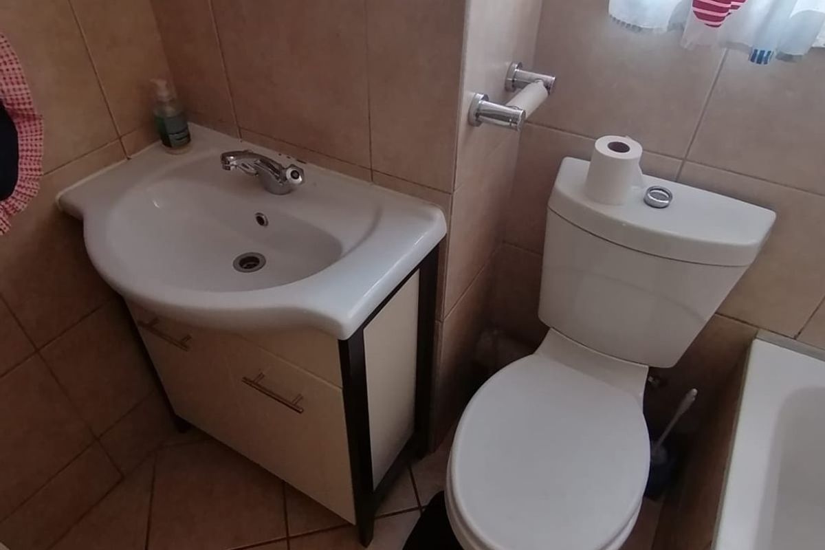 A functional bathroom featuring a vanity basin, toilet, and bathtub with neutral wall and floor tiling.