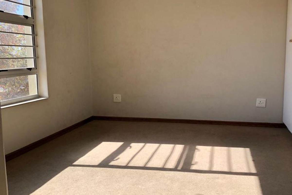 An empty bedroom featuring carpeted flooring, louvered windows, and neutral wall finishes, providing a blank canvas for potential interior design updates.