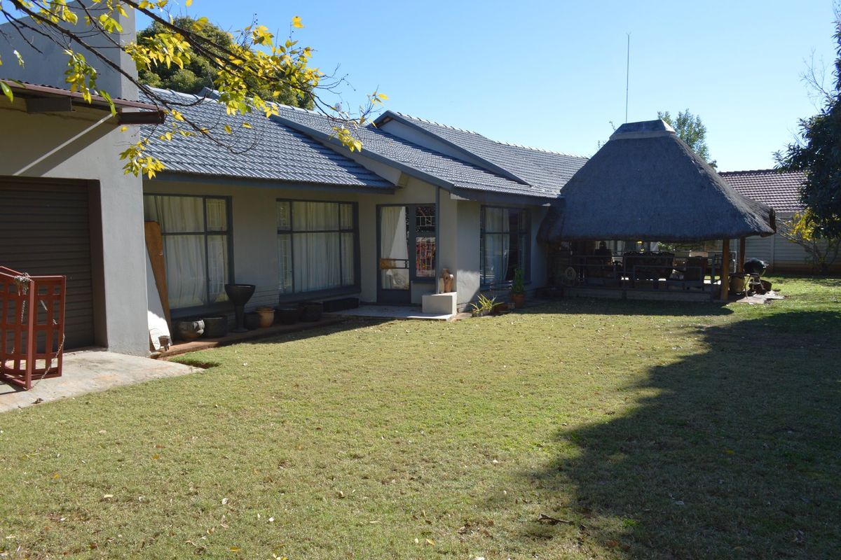 Rear view of the house featuring a spacious lawn, paved patio area, and a traditional thatched lapa for outdoor entertainment.