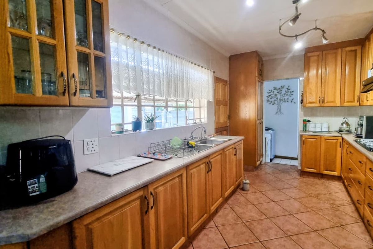 A functional kitchen featuring traditional wooden cabinetry, laminate countertops, a double bowl sink, and tiled flooring with an adjacent utility area.