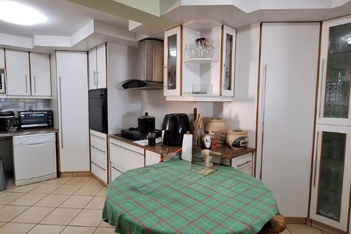 A functional kitchen featuring white built-in cabinetry, tiled flooring, and integrated appliances, offering a practical layout with ample storage space.