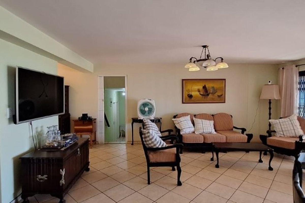 A spacious living room featuring tiled flooring, a central ceiling light fixture, and large sliding glass doors providing access to the outdoor area.