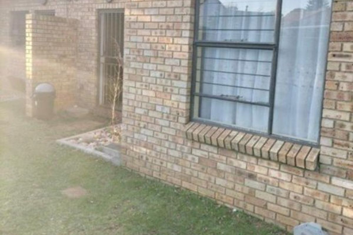 Rear exterior view of the apartment featuring face brick walls, security bars on windows, and a small garden area.