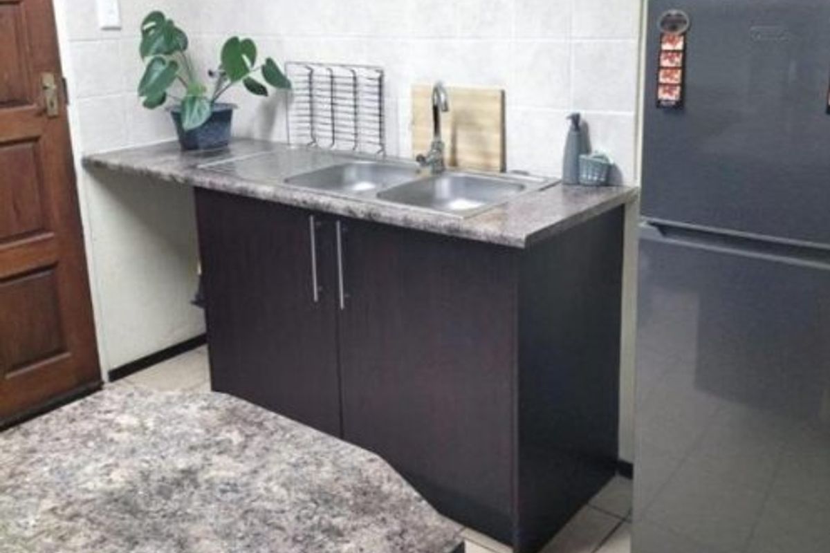 A compact kitchen area featuring dark wood cabinetry, a double bowl stainless steel sink, laminate countertops, and neutral tiled splashbacks.