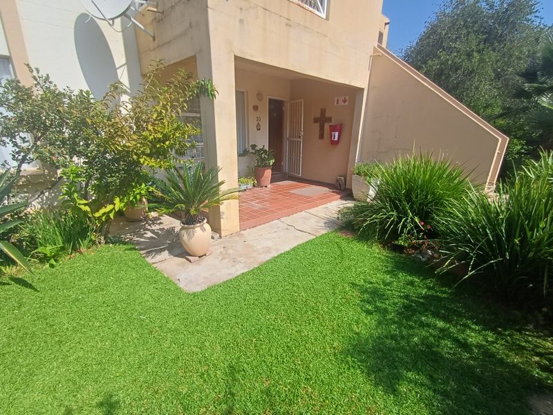 Front entrance of the apartment featuring a covered tiled patio, concrete walkway, and small private garden area.