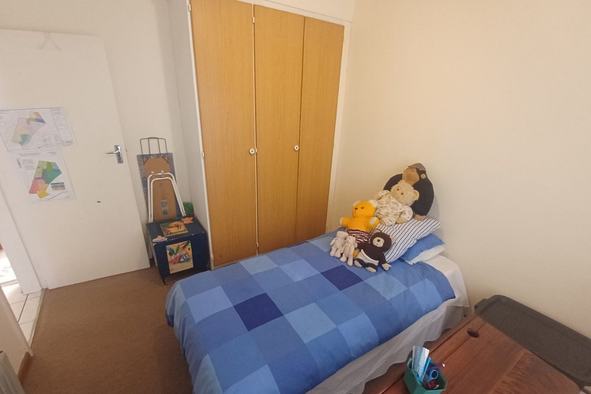A functional bedroom featuring a built-in wooden wardrobe and carpeted flooring, offering a practical space for a single bed.