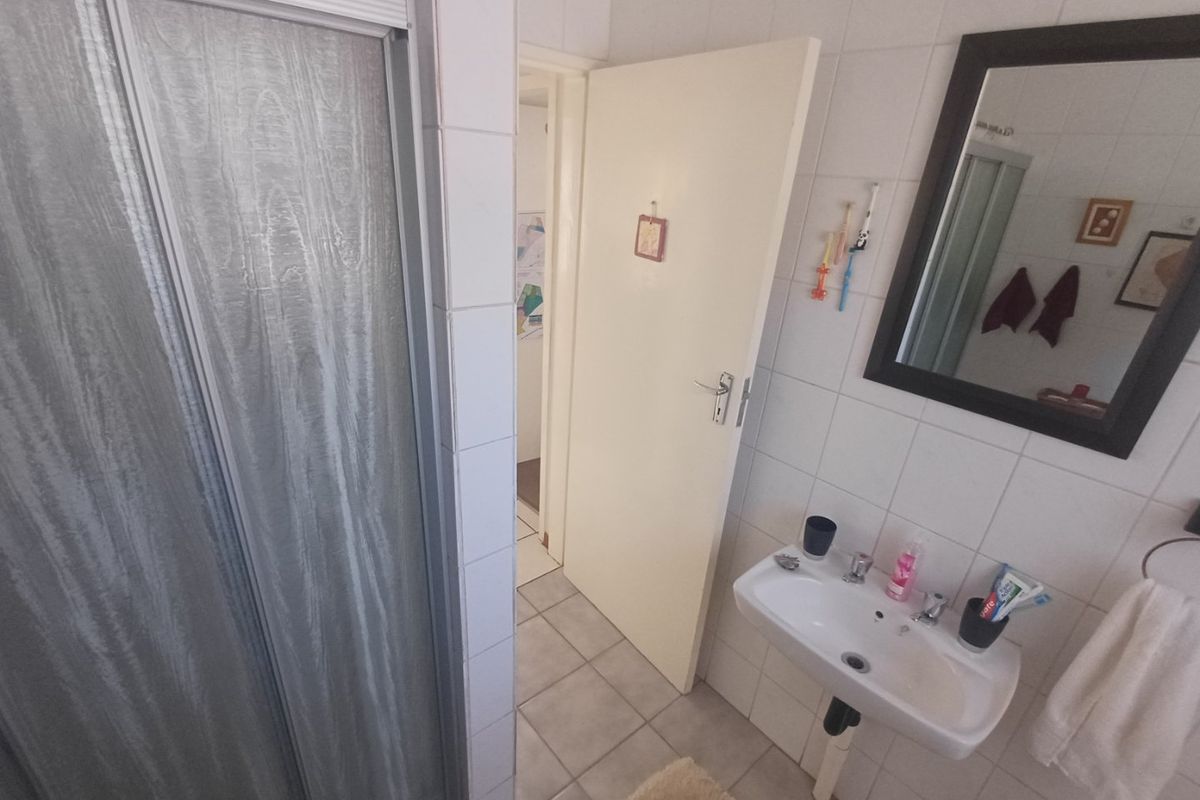 A functional bathroom featuring a shower enclosure, wall-mounted basin, and neutral tiled finishes throughout.