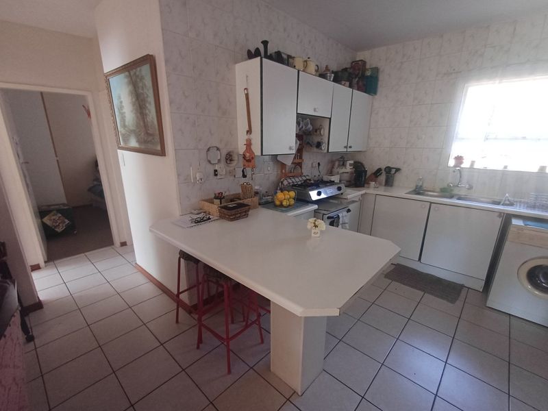 A functional kitchen featuring white cabinetry, tiled backsplash, a breakfast bar, and tiled flooring with direct access to the hallway.