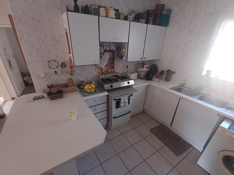 A functional kitchen featuring white cabinetry, a gas hob, oven, double sink, and a breakfast nook with tiled finishes throughout.