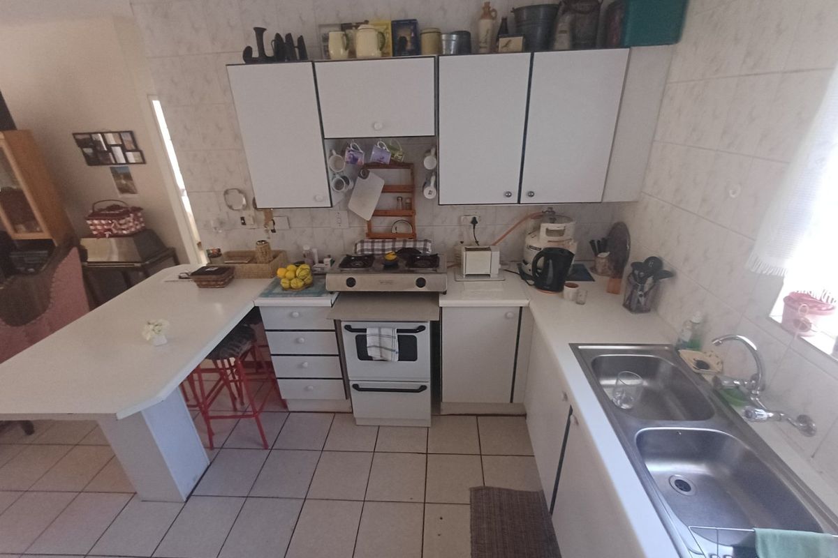 A functional kitchen featuring white cabinetry, a gas hob, oven, double stainless steel sink, and a breakfast bar with tiled flooring and splashbacks.