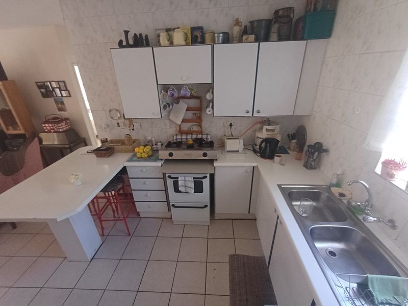 A functional kitchen featuring white cabinetry, a gas hob, oven, double stainless steel sink, and a breakfast bar with tiled flooring and splashbacks.