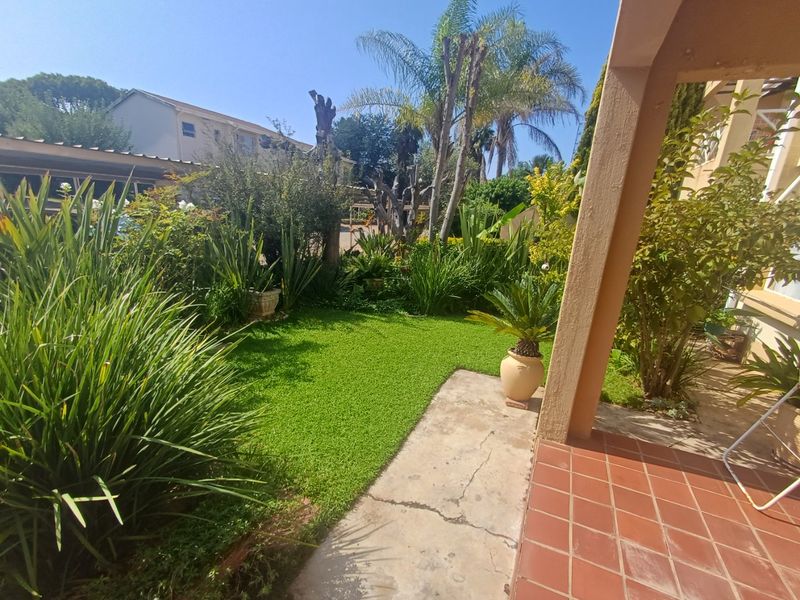 A well-maintained garden area featuring a tiled patio, concrete pathway, and established greenery, providing a pleasant outdoor space.